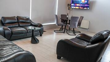 A modern living room with leather sofas, a glass coffee table, and a flat-screen TV mounted on the wall.