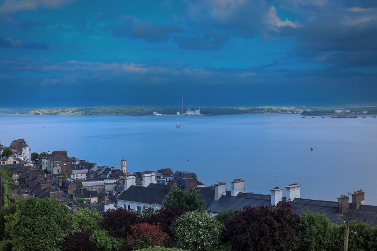 A coastal town with buildings along the waterfront, a large body of water, and a distant industrial structure.