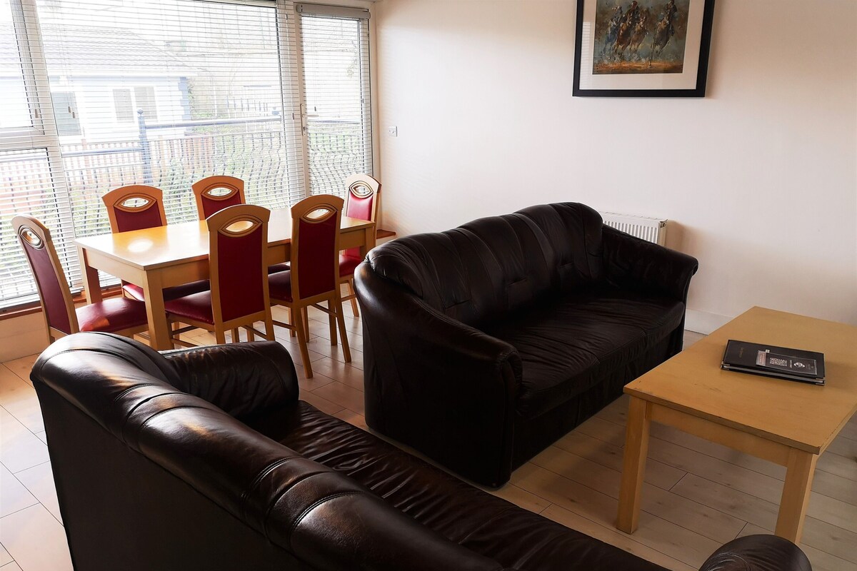 A living room with a black leather sofa, a wooden coffee table, and a dining table with red chairs.
