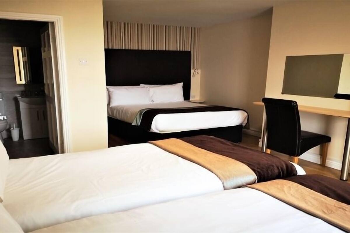 A hotel room with two beds, a desk, a chair, a TV, and a bathroom visible through an open door.