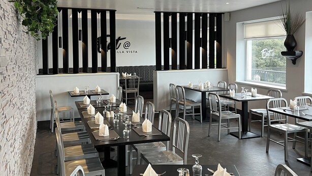 A modern restaurant with long tables, metal chairs, and a hanging plant.