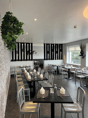 Un restaurant modern amb taules llargues, cadires metàl·liques i una planta penjant.