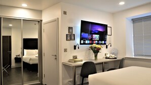 A hotel room with a bed, a desk with a computer monitor, a chair, and a window with blinds.