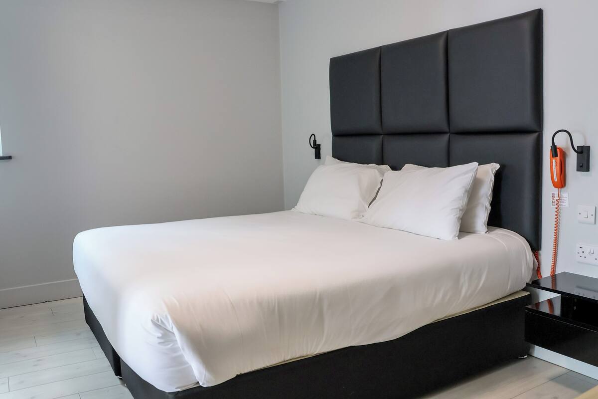 A modern bedroom with a large bed, a black headboard, and a bedside telephone.