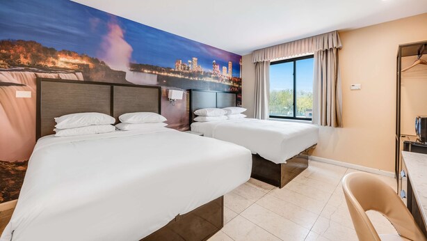 Une chambre d’hôtel avec deux lits, une grande fenêtre et une fresque représentant une cascade et le panorama d’une ville.