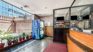 Un hall d’hôtel comprenant un comptoir d’accueil, un distributeur automatique, des plantes en pot et un escalier.