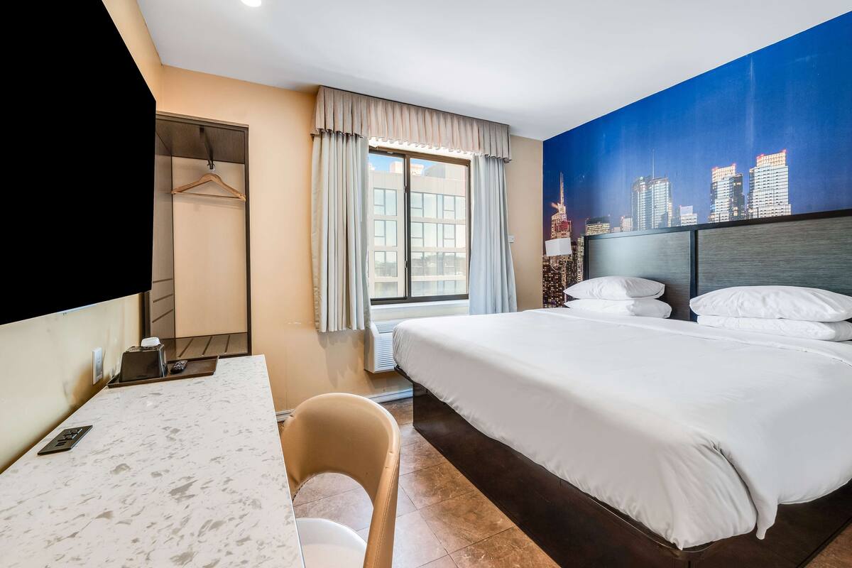 Ein Hotelzimmer mit Bett, Schreibtisch, Stuhl, Kleiderschrank und einer Stadtszenen-Mural an der Wand.