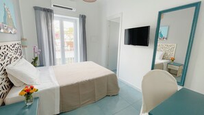 A hotel room with a bed, a desk, a chair, a TV, and a window with curtains. - Hotel Lord Byron (Forio)