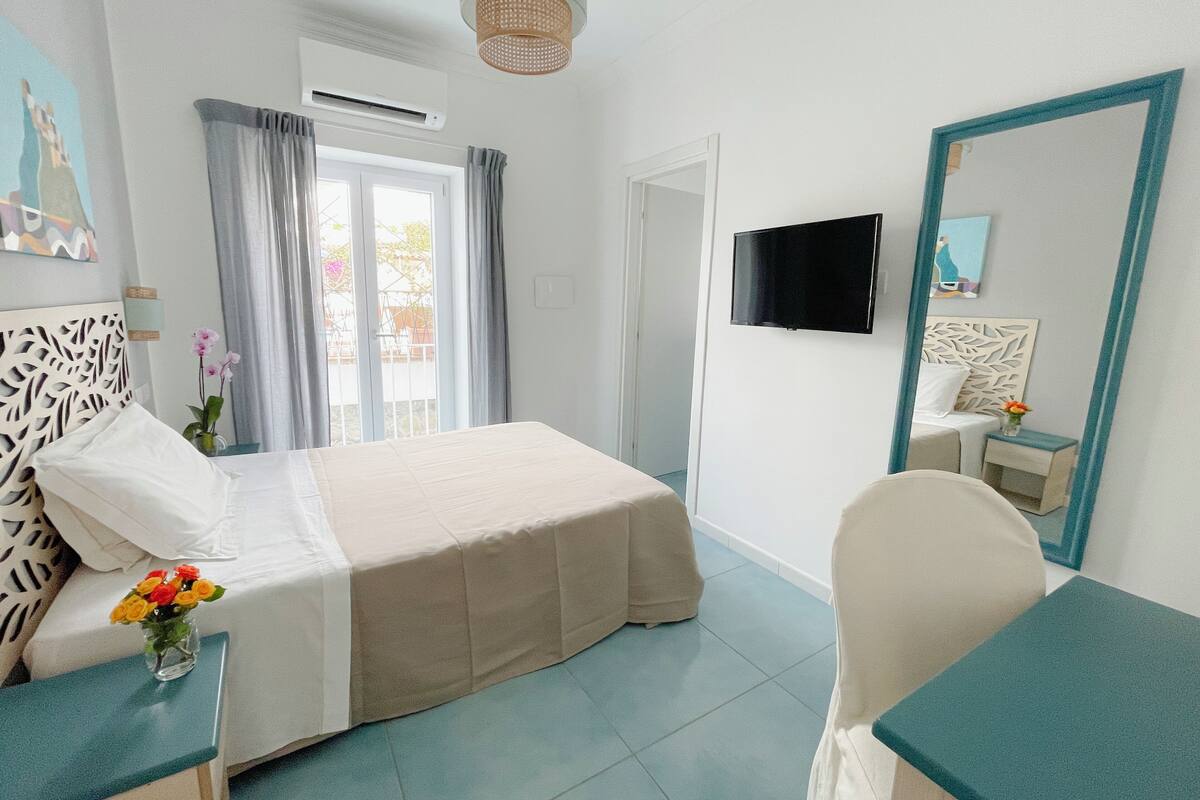 Une chambre d’hôtel avec un lit, un bureau, une chaise, une télévision et une fenêtre avec des rideaux.