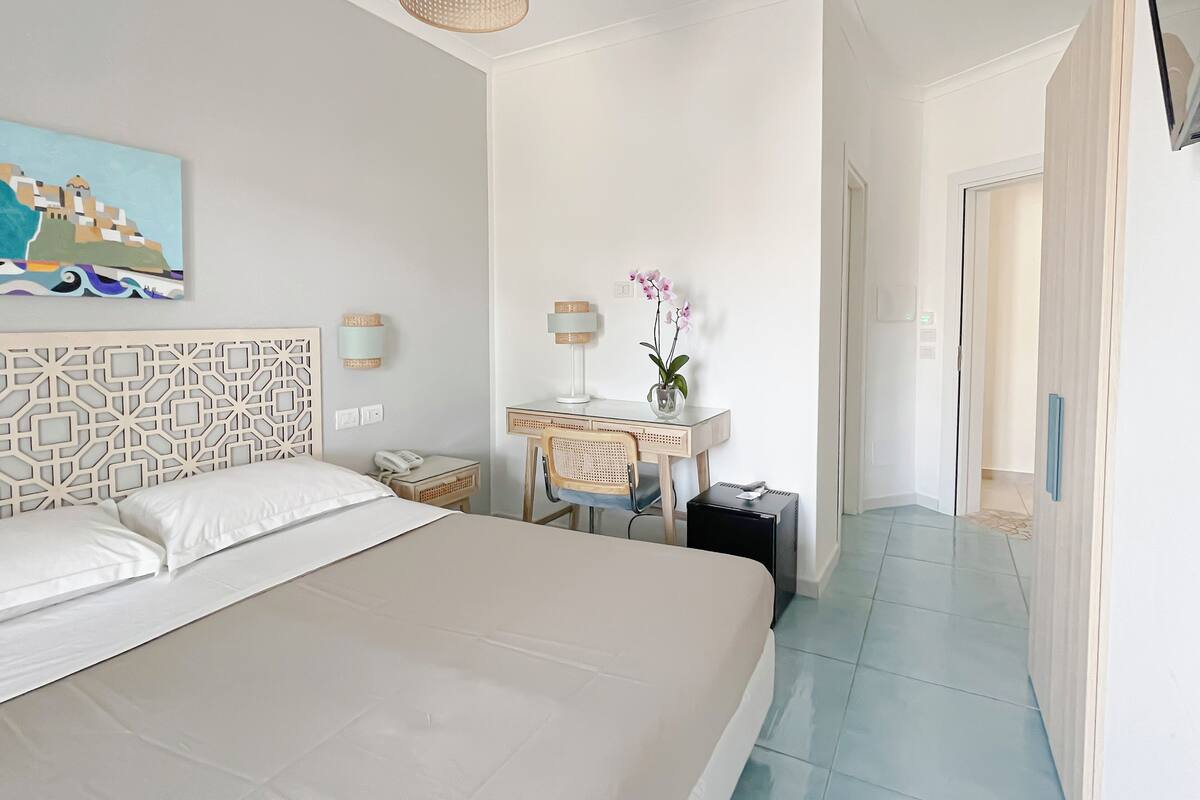 Une chambre d’hôtel avec un grand lit, un bureau avec un ordinateur, un téléphone et un vase rempli de fleurs.