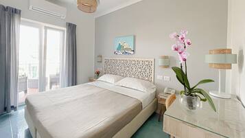 A hotel room with a large bed, a bedside table with a phone, a vase with flowers, and a painting on the wall.
