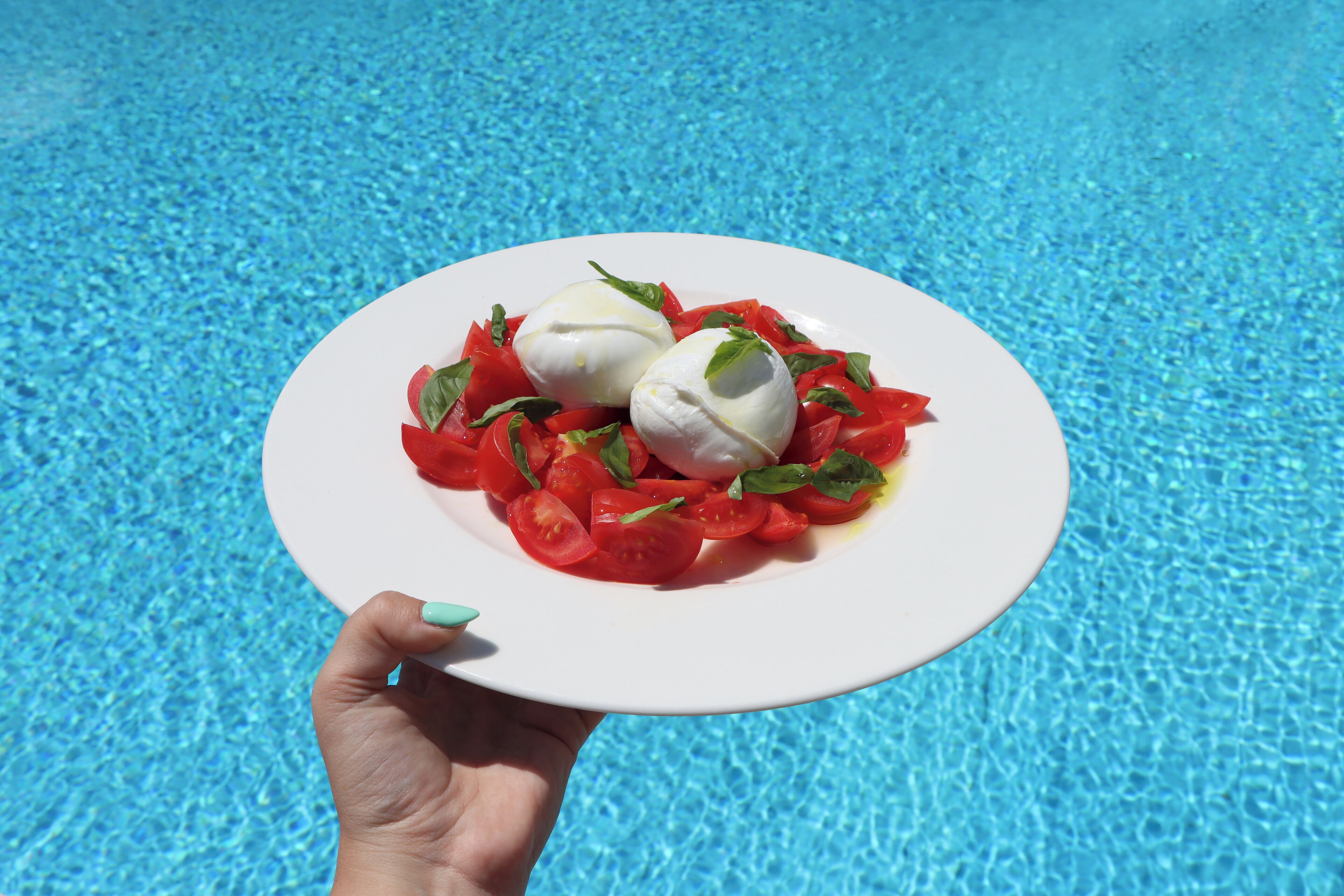 Ein Teller mit Mozzarella-Kugeln und Tomatenscheiben, der über einem Pool schwebt.