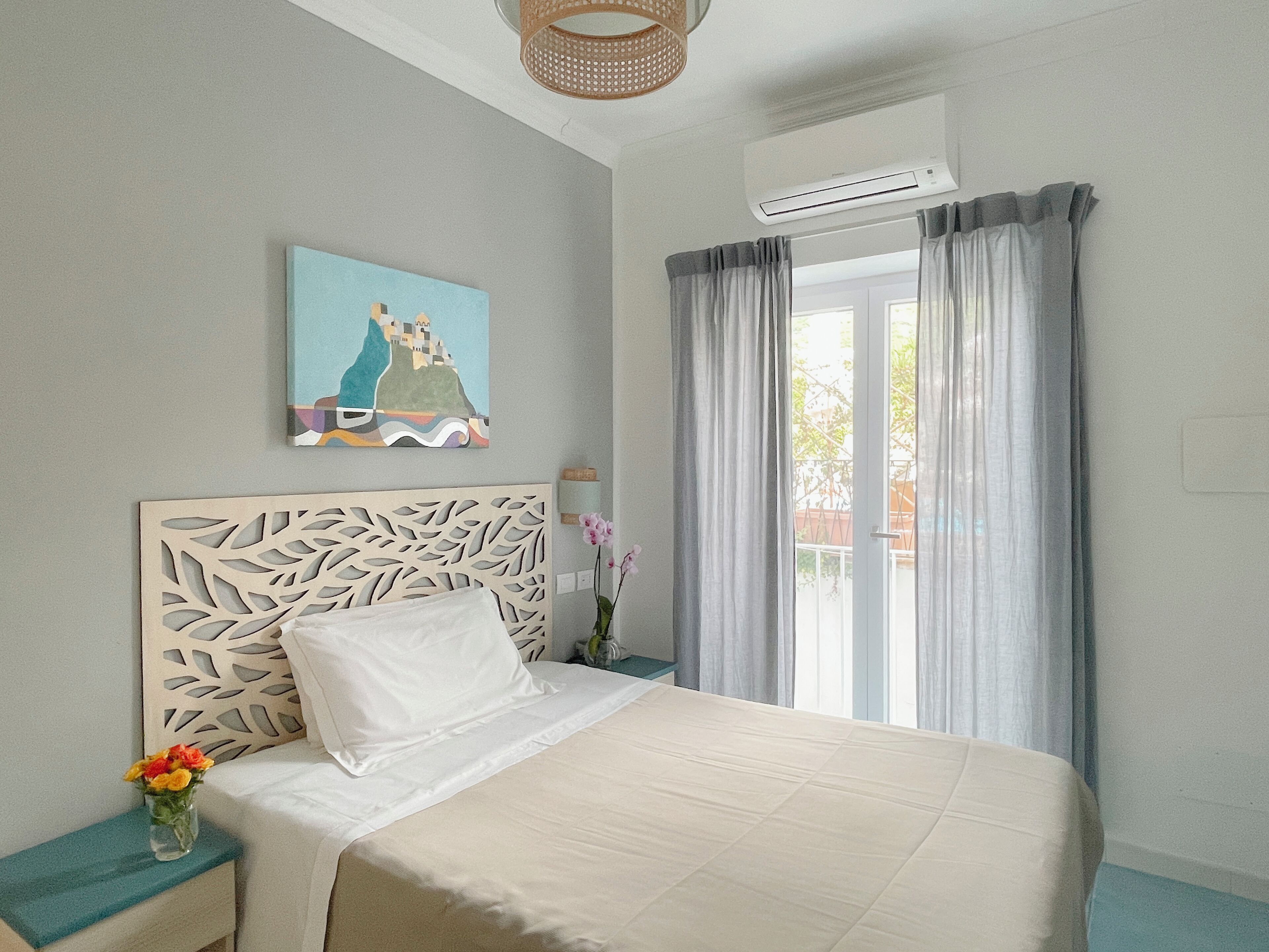 Une chambre à coucher avec un lit, un climatiseur fixé au mur, une fenêtre avec des rideaux et un tableau accroché au mur.