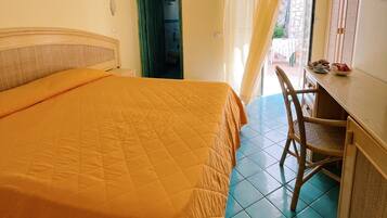 Une chambre avec un grand lit, un bureau et une chaise. Il y a une porte qui donne sur une autre pièce et une fenêtre avec des rideaux.