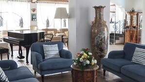 A living room with a grand piano, two blue sofas, a large vase, and a wooden cabinet. - Hotel Lord Byron (Forio)