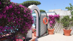 A gated entrance with a white archway, potted plants, and a lifebuoy on a tiled patio. - Hotel Lord Byron (Forio)
