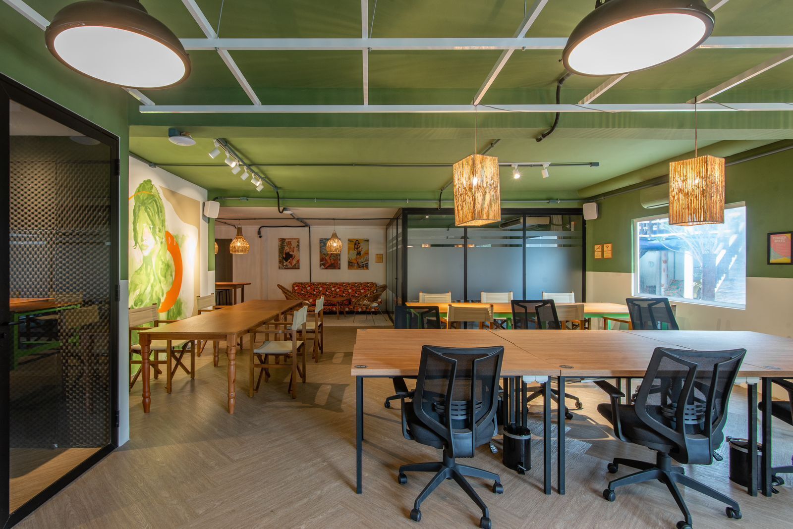 A modern meeting room with a large wooden table, black office chairs, and hanging wicker lamps.