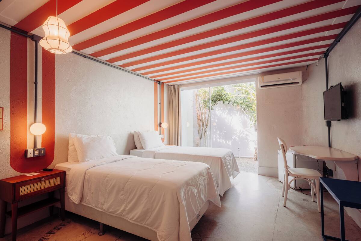 Habitación de hotel con dos camas, un escritorio, una silla, un televisor y una ventana con vistas a la vegetación.