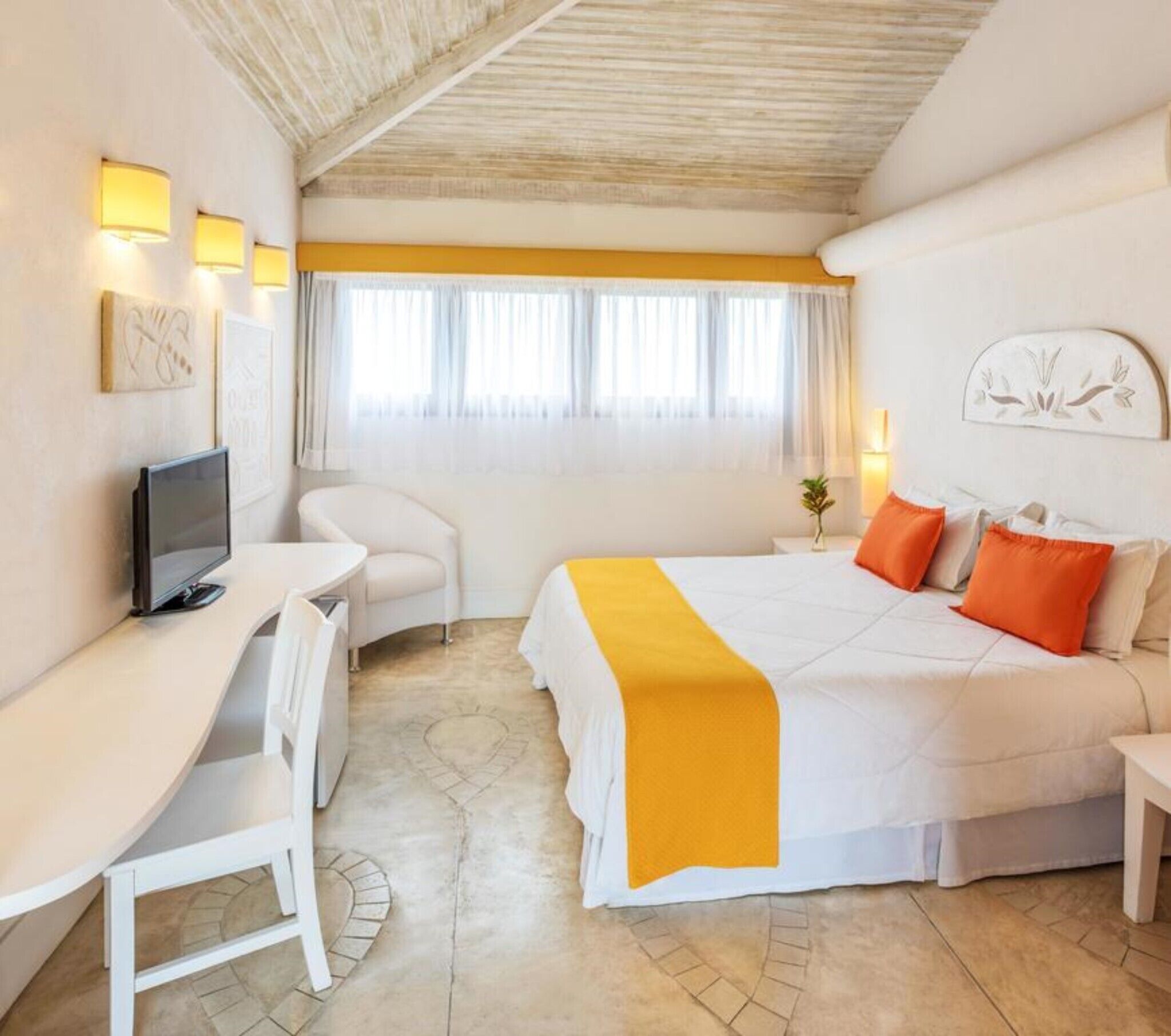 A hotel room with a bed, a desk, a chair, a television, and a window with curtains.