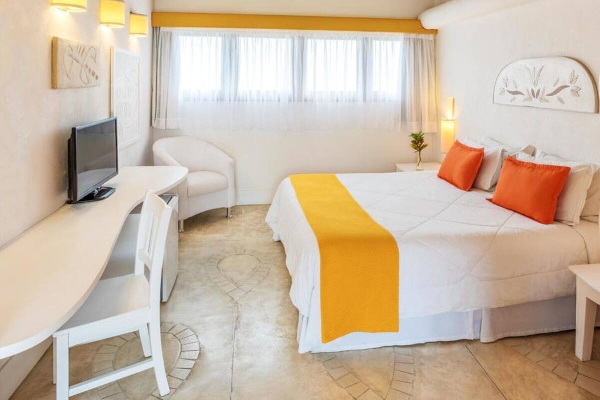 A hotel room with a bed, a desk, a chair, a television, and a window with curtains.