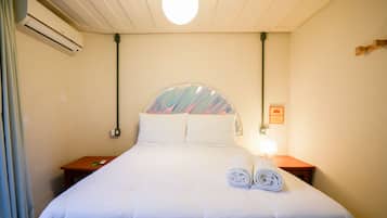 A hotel room with a bed, a nightstand, an air conditioning unit, and a wall-mounted lamp.