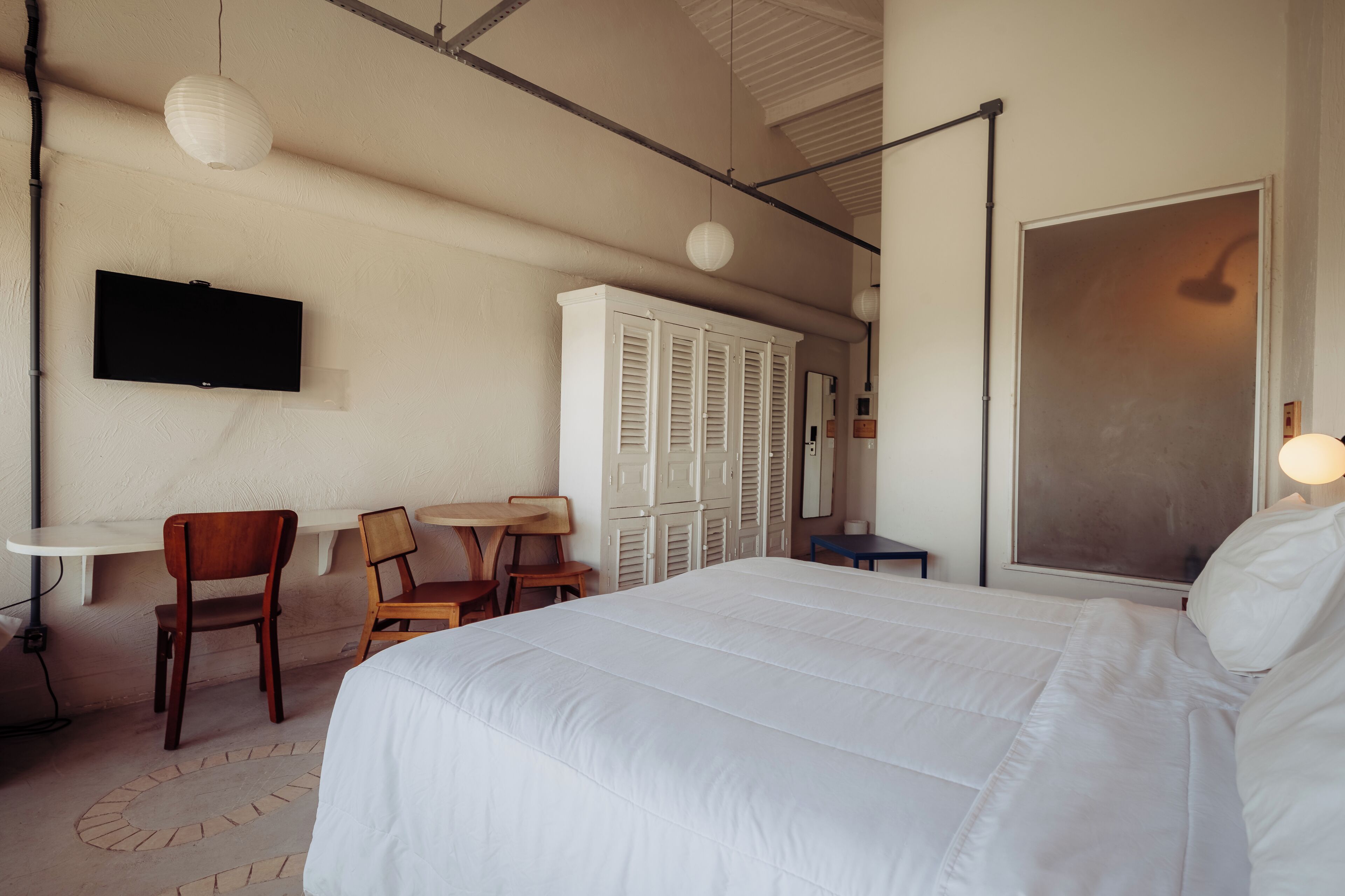 Une chambre d’hôtel avec un grand lit, un bureau avec des chaises, une télévision et une armoire.