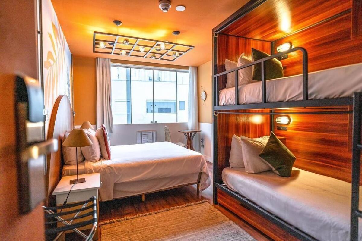 A room with a bunk bed, a desk with a lamp, a chair, a window with curtains, and a ceiling light fixture.