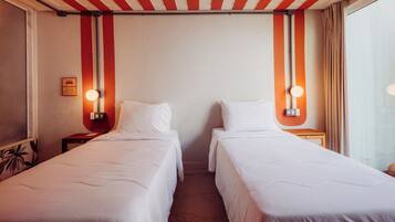 A hotel room with two single beds, a red and white striped ceiling, and wall-mounted lamps.