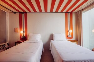 Habitación de hotel con dos camas individuales, techo a rayas rojas y blancas, y lámparas fijadas a la pared.