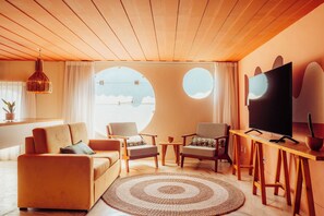 A modern living room with a sofa, two armchairs, a coffee table, a TV, and a large window with curtains. - Own Buzios Beach Hotel (Búzios)