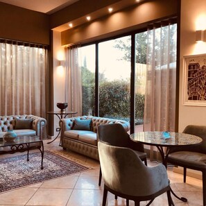 A modern living room with a sofa, armchairs, a coffee table, and a view through large windows. - Hotel Duca della Corgna (Castiglione del Lago)