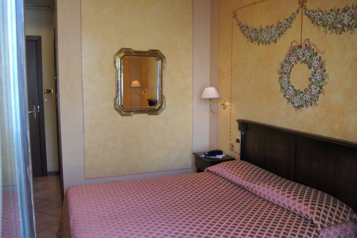 A hotel room with a bed, a nightstand, a mirror, and a wall with a floral wreath.