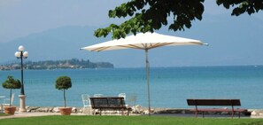 A seaside view with a bench, a table with chairs, and an umbrella. - Hotel Lugana Parco Al Lago (Sirmione)