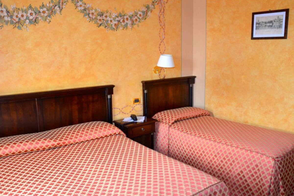 A room with two beds, a nightstand, a lamp, and a floral wall decoration.