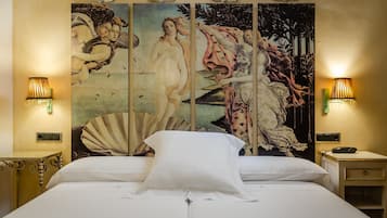 A bed with white linens, flanked by two nightstands with lamps, and a large, ornate tapestry on the wall behind.