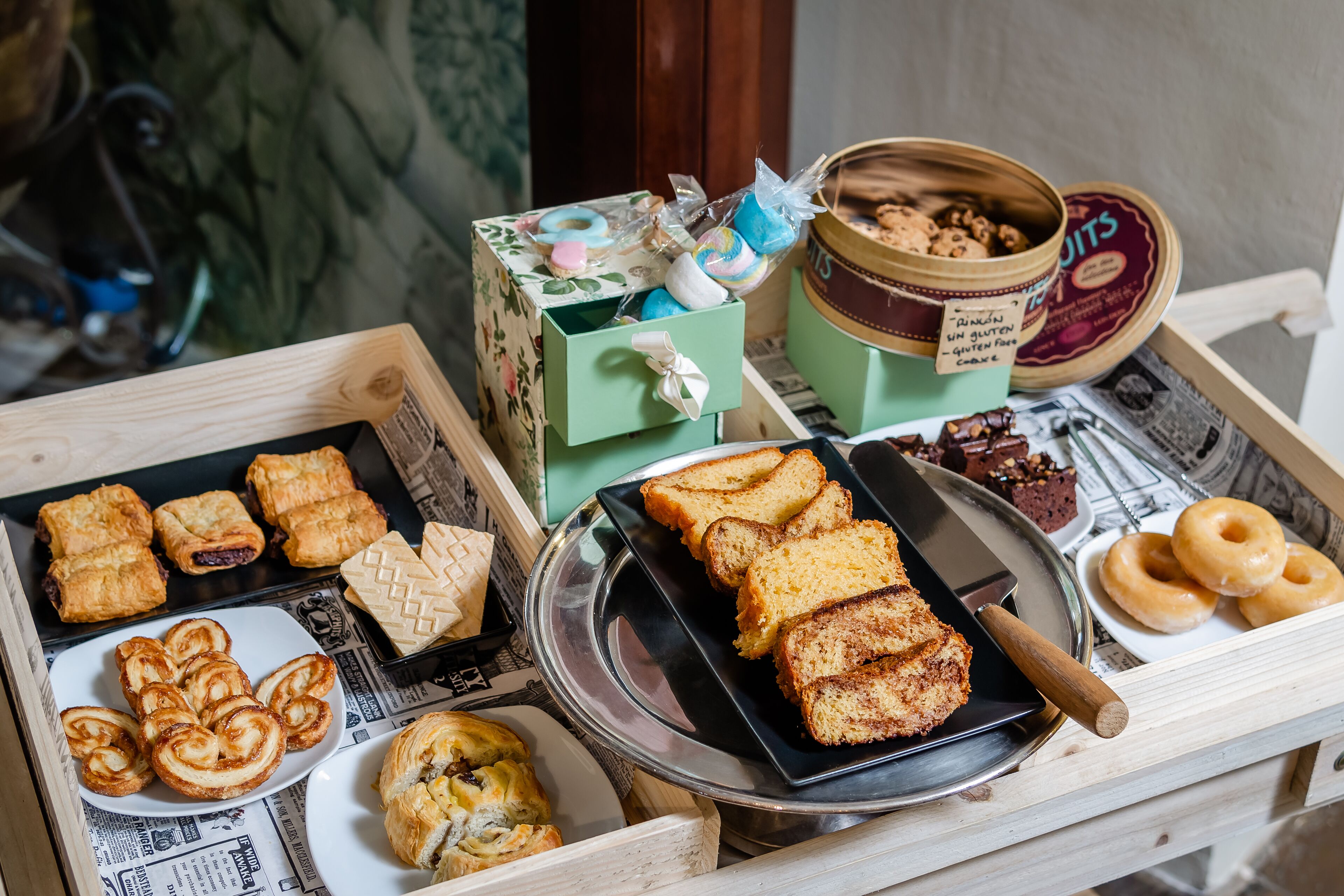 A variety of baked goods displayed on a wooden table, including pastries, bread, and donuts.