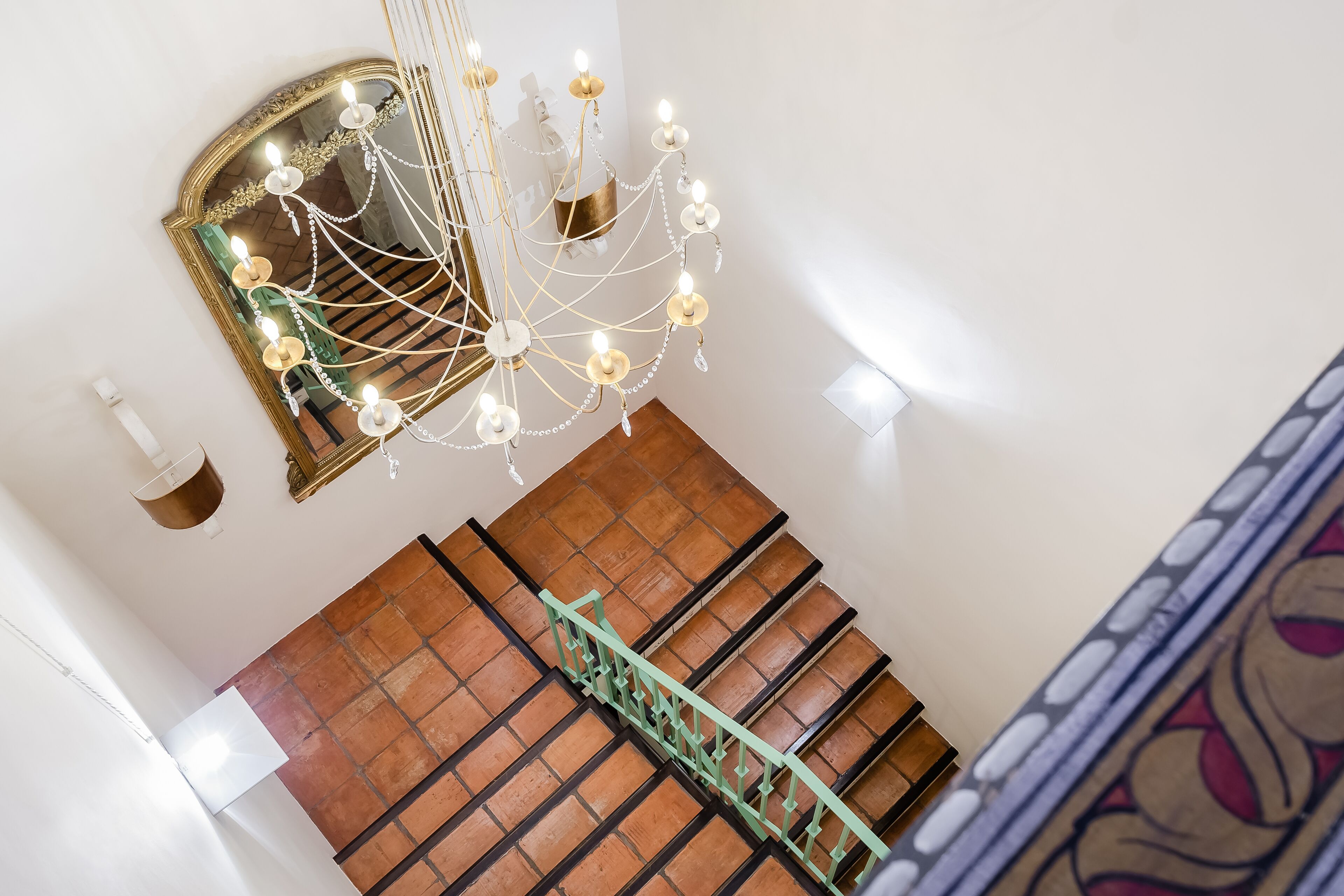 A staircase with a green railing, a chandelier, and a mirror on the wall.