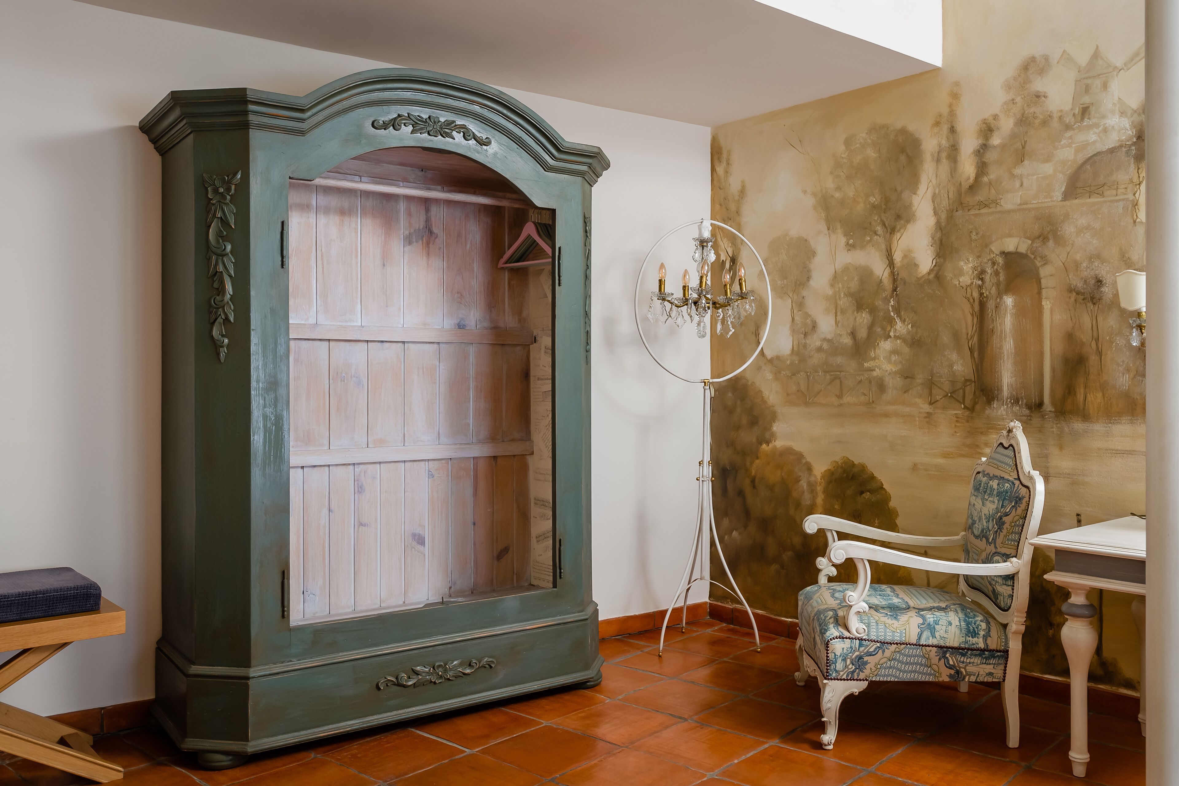 A room with a large wooden wardrobe, a white chair, a small table, and a wall mural.