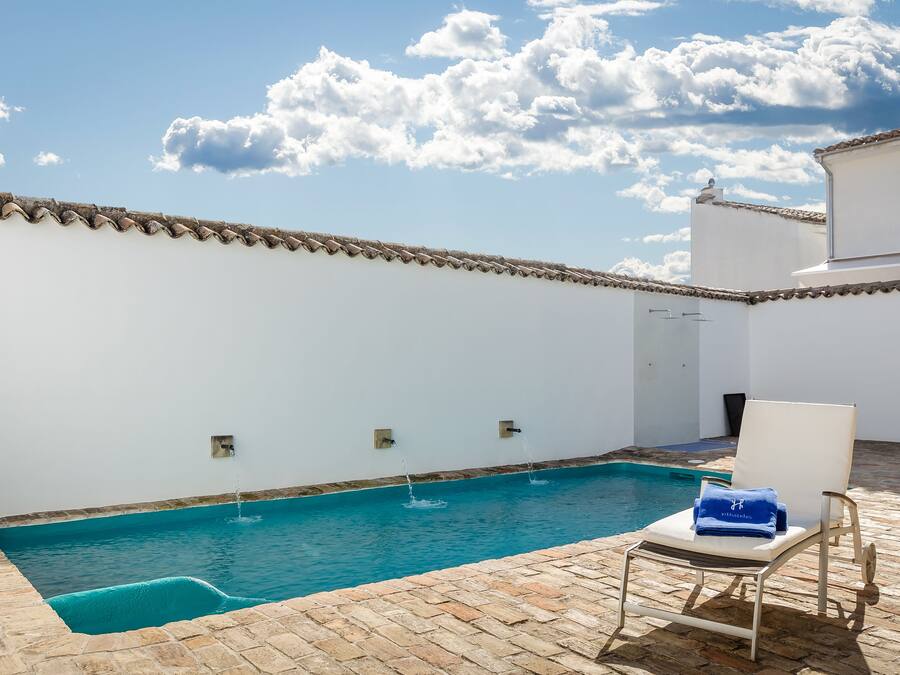 Una piscina con borde de azulejos, una pared blanca y una toalla azul sobre una silla.