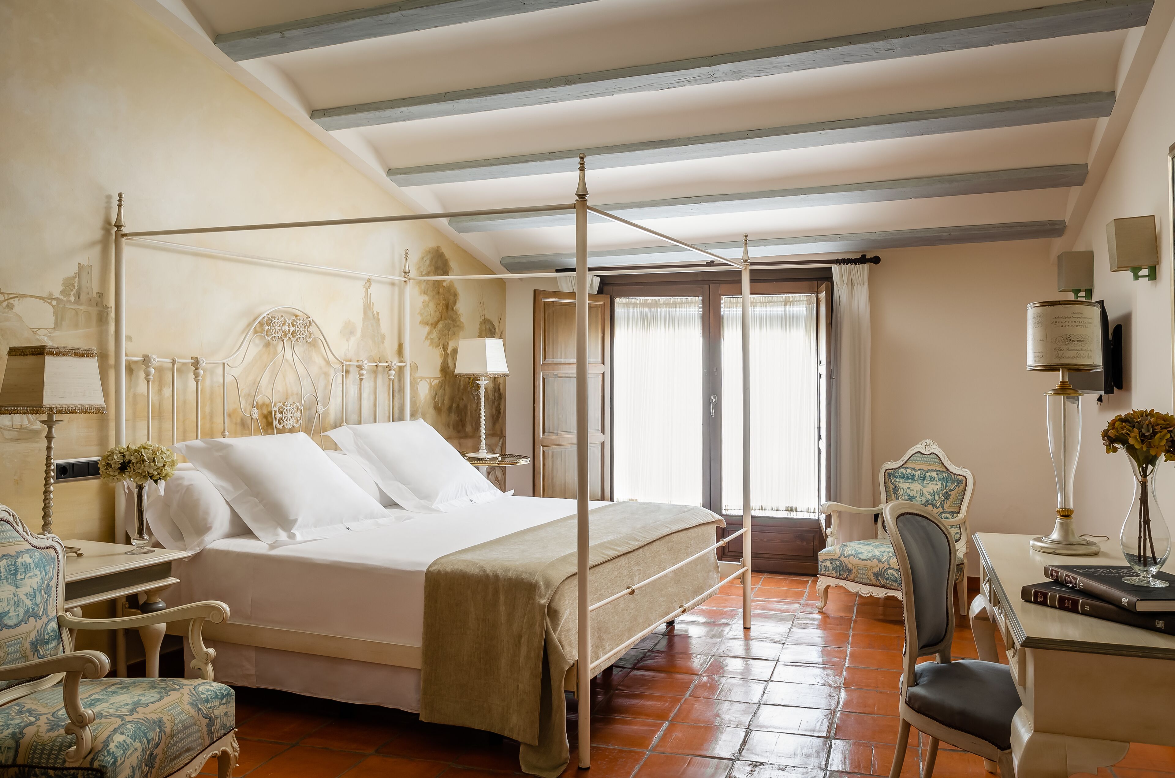 Una cama con dosel y un cabecero, un escritorio con lámpara, una silla y una ventana con cortinas.