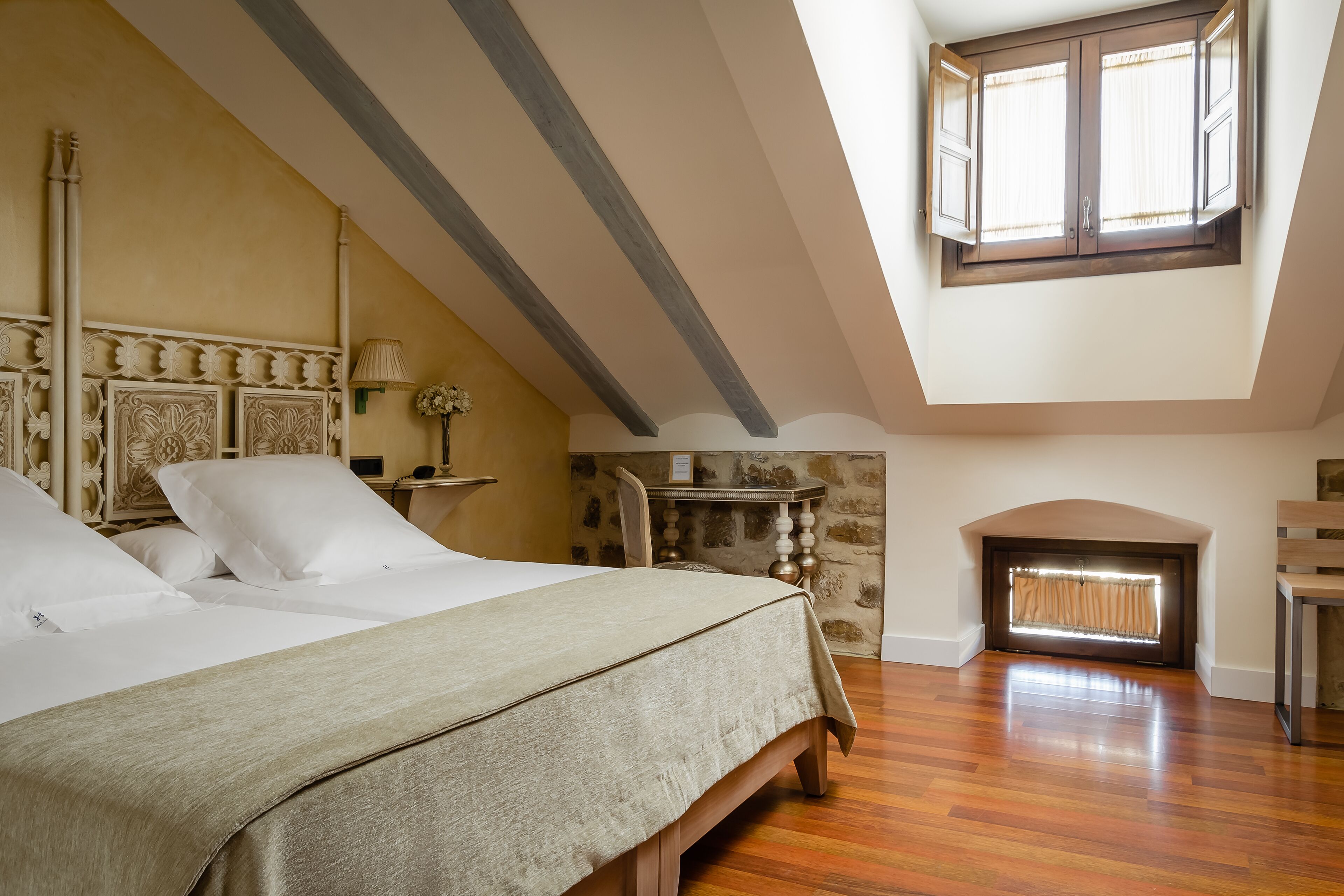 Un dormitorio con cama, pared de piedra, chimenea y ventana con cortinas.