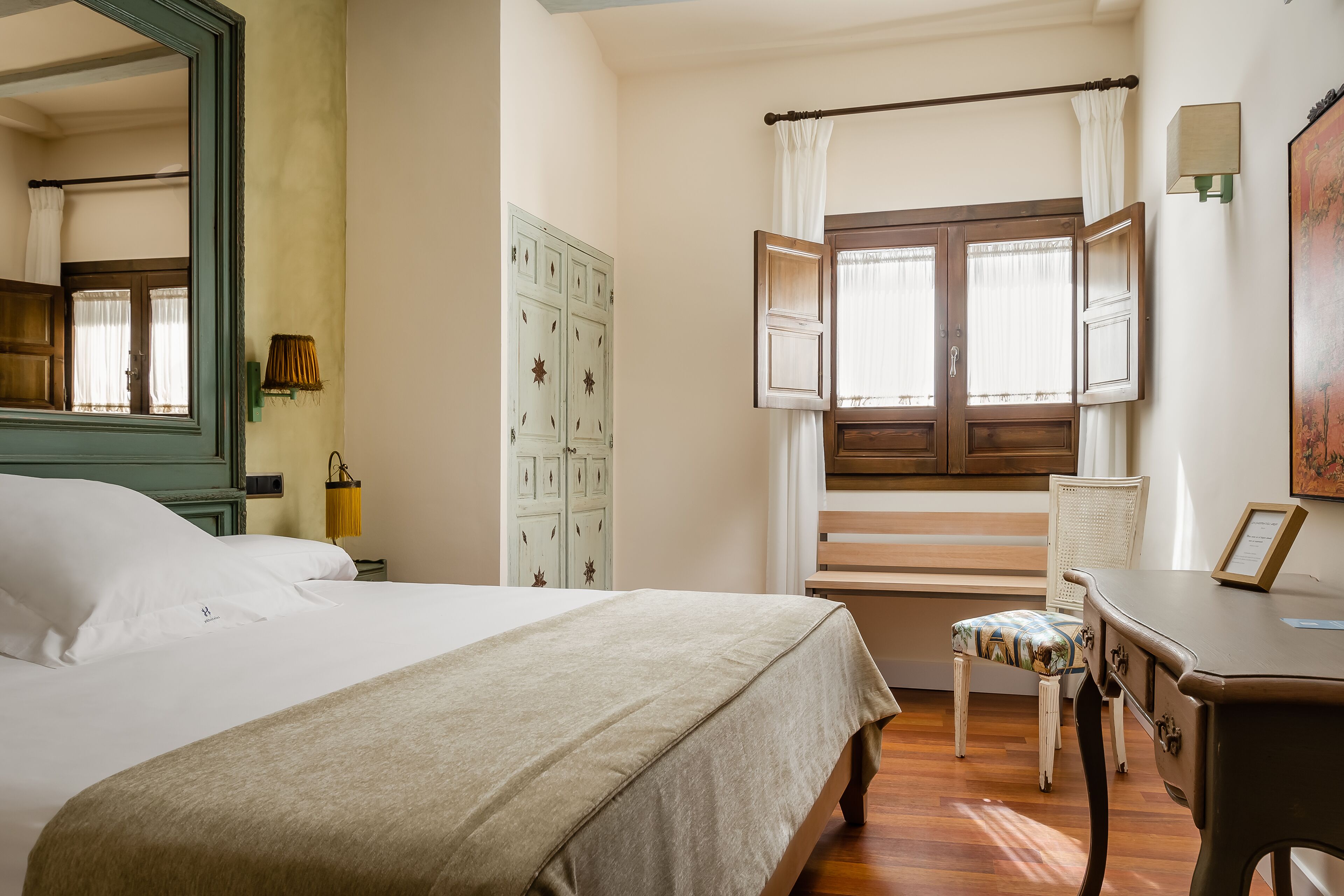 Un dormitorio con cama, una silla, un escritorio, un armario y una ventana con cortinas.