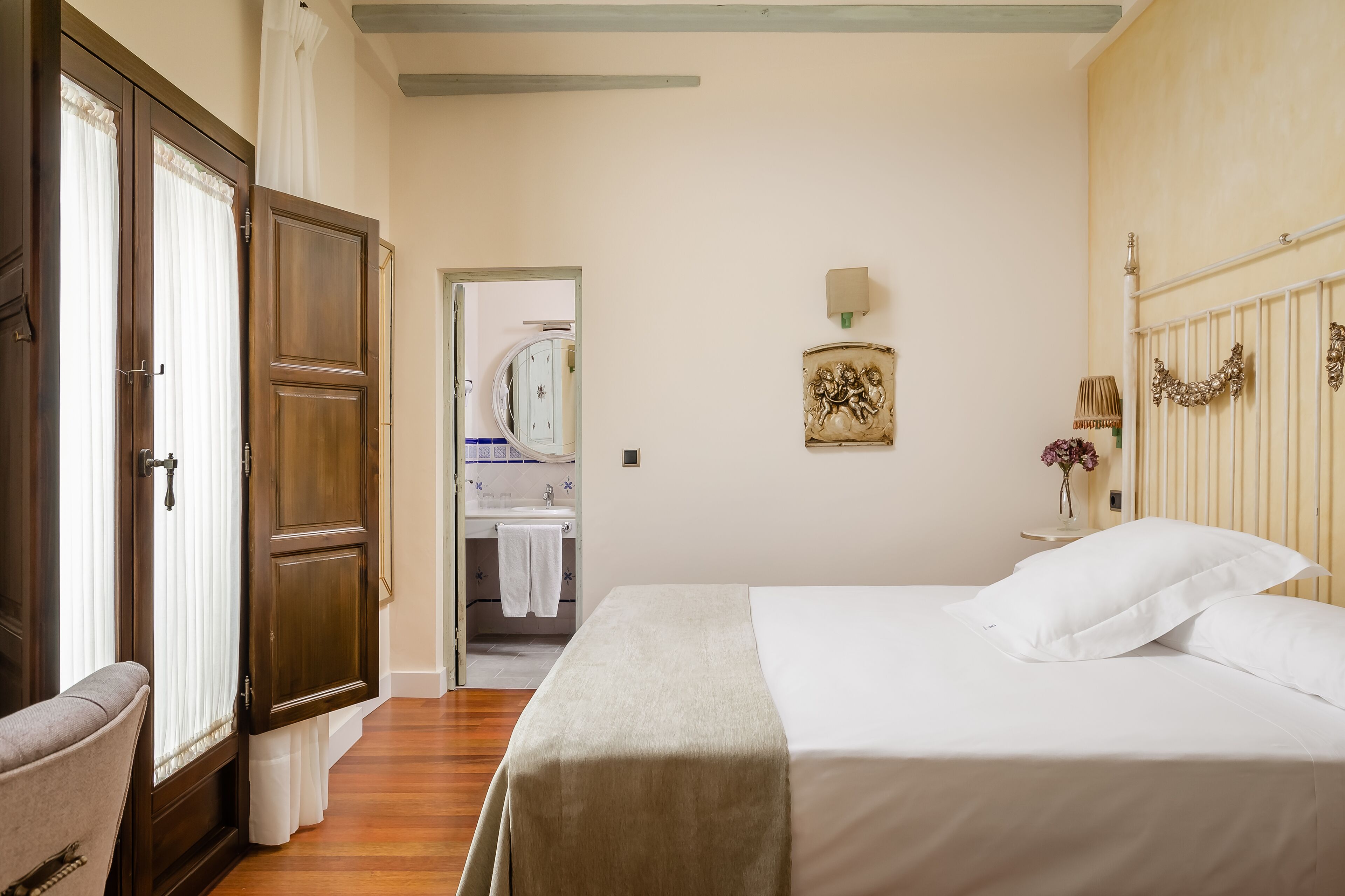 A bedroom with a bed, a nightstand, a wall-mounted lamp, and a door leading to a bathroom.