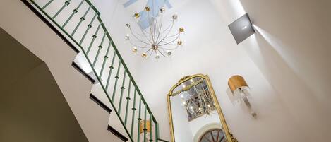 A staircase with green railings, a chandelier, and a mirror with a wooden frame.