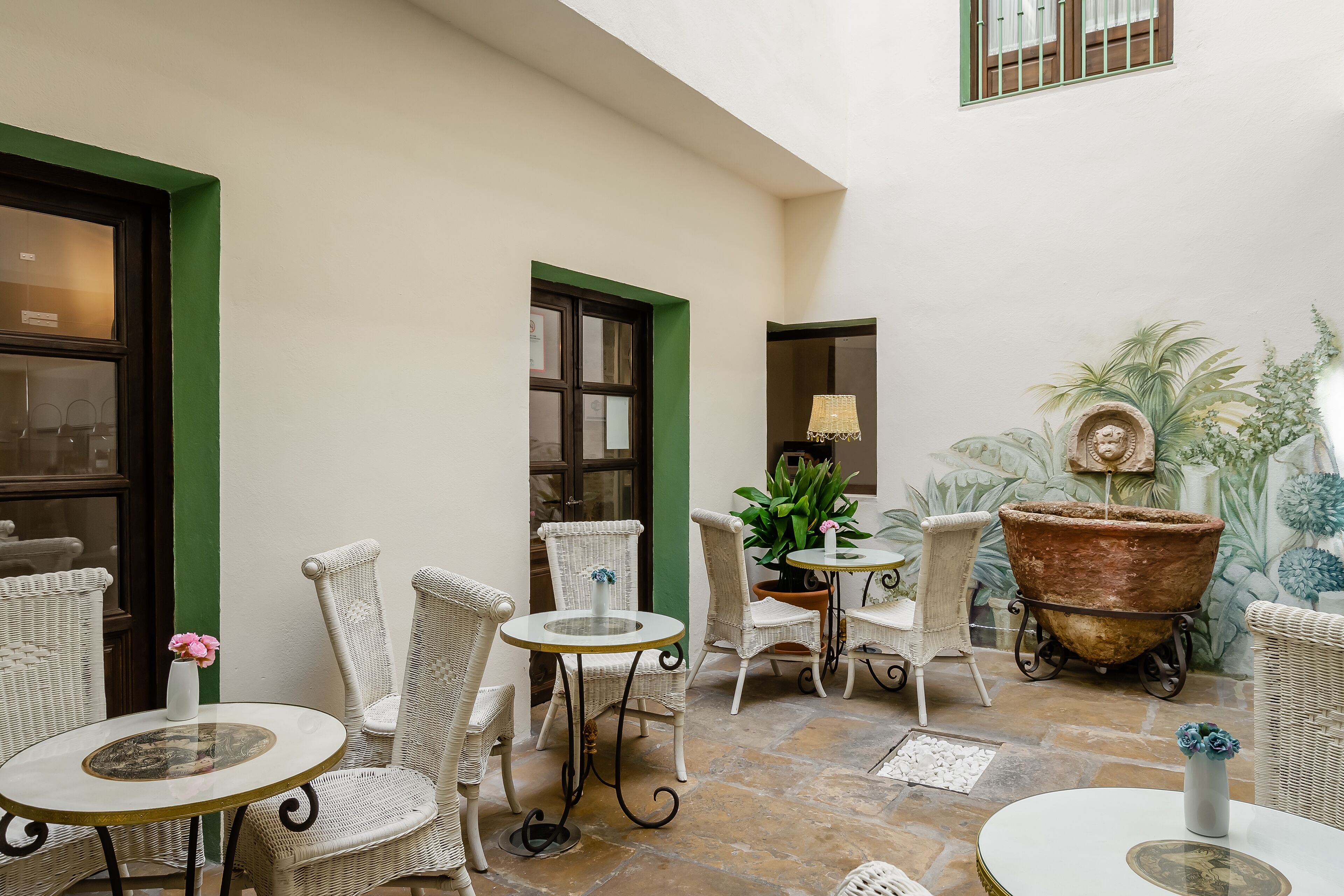 A courtyard with wicker furniture, a large planter, and a mural on the wall.
