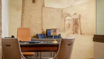 Una sala de estudio con un escritorio, dos sillas, una estantería llena de libros y un mural de una escena arquitectónica.