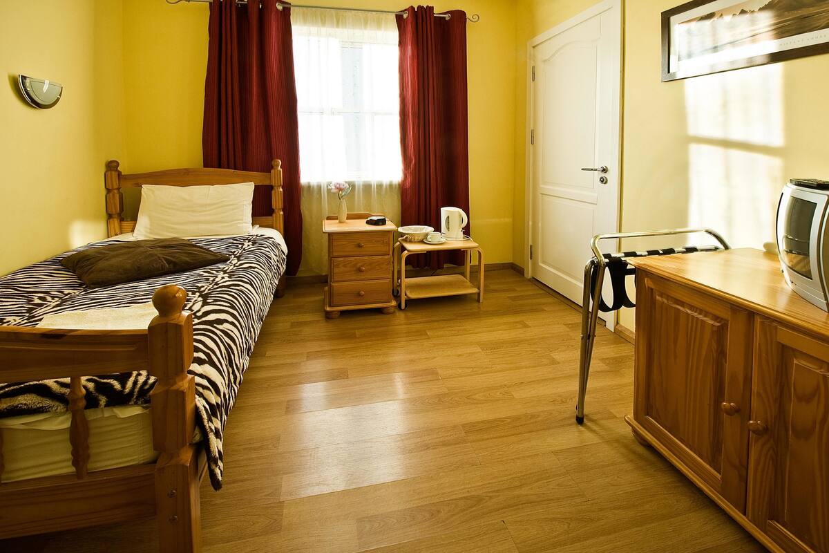 Een slaapkamer met een houten bed, nachtkastje, stoel, kledingkast en een raam met gordijnen.