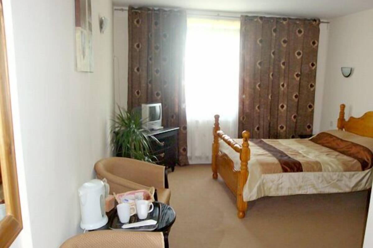 Een hotelkamer met een bed, een stoel, een bureau met een televisie en een raam met gordijnen.