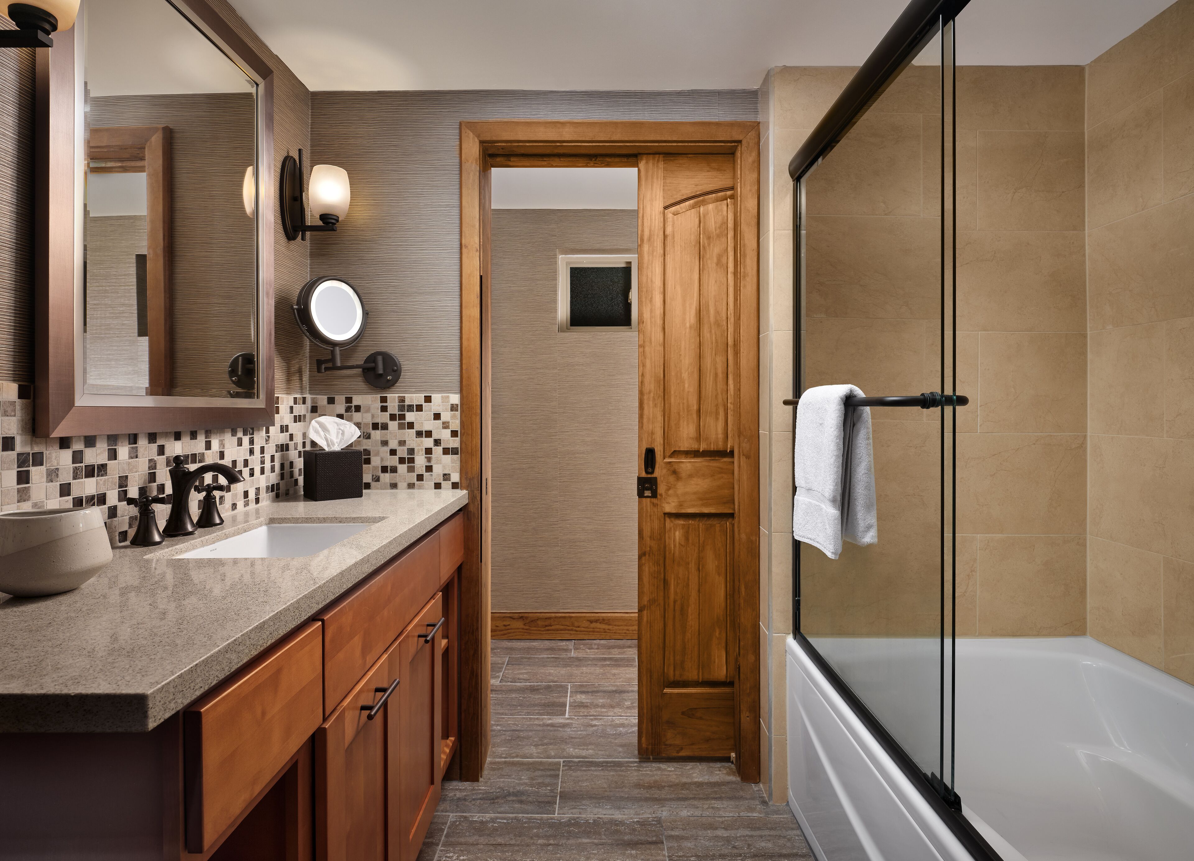 A modern bathroom with a wooden door, a glass shower enclosure, and a vanity with a large mirror and two sinks.
