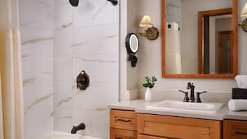 A bathroom with a bathtub, a sink with a mirror, wooden cabinets, and a towel rack.